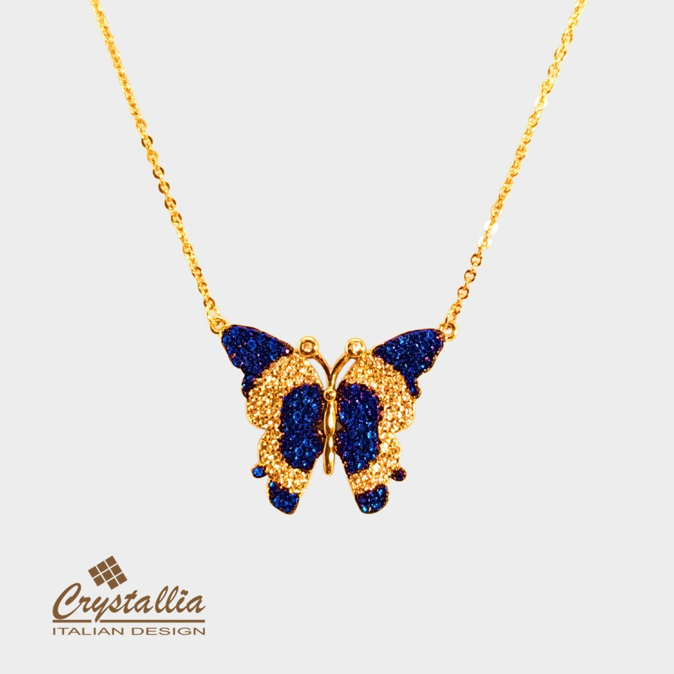 Butterfly-shaped necklace with blue gemstones and gold accents on a white background, featuring the Crystallia brand.