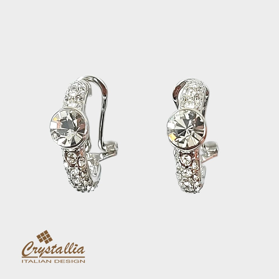 Pair of silver hoop earrings with clear gemstones on a light gray background, featuring the Crystallia brand.