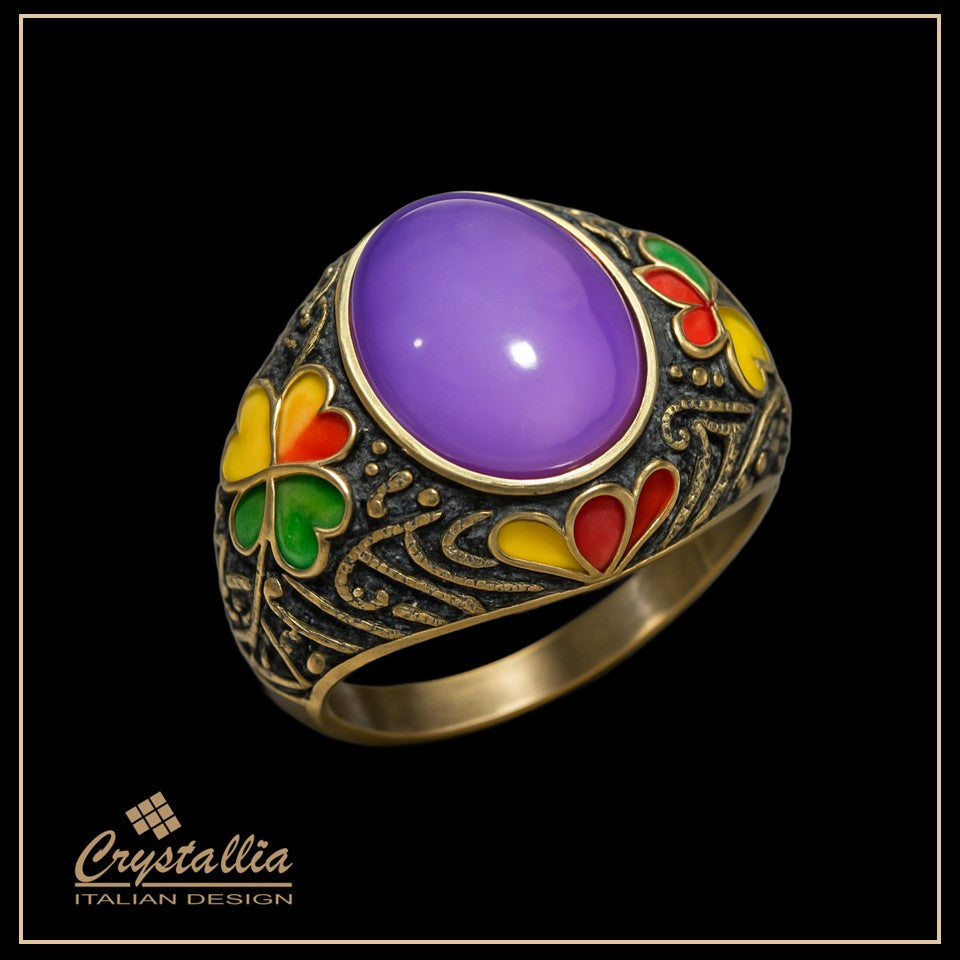 Gold ring with a purple gemstone and colorful accents on a black background, featuring the Crystallia brand.