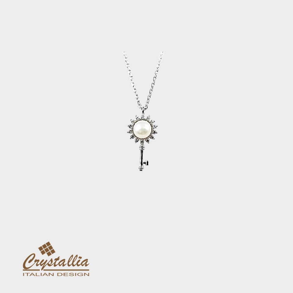 Silver key-shaped pendant with pearl on a white background, featuring Crystallia brand logo.