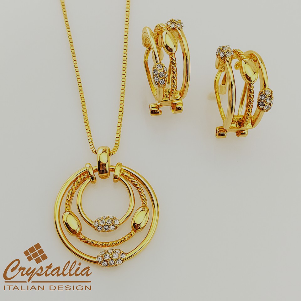 Gold jewelry set with necklace and earrings on a light gray background, featuring the Crystallia brand.