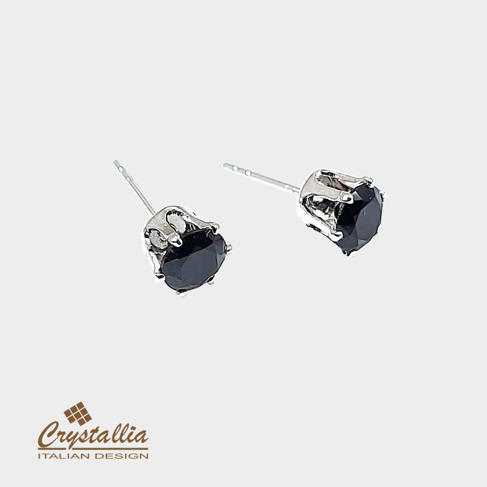 Pair of black heart-shaped gemstone earrings with silver settings on a light gray background, featuring the Crystallia brand.