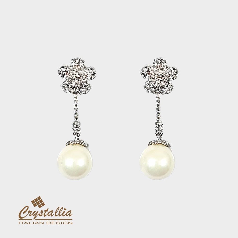 Pair of pearl earrings with decorative tops on a light gray background, featuring the Crystallia brand.