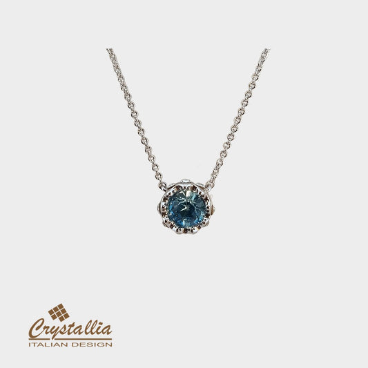 Silver necklace with a blue gemstone pendant on a white background, featuring the Crystallia brand.