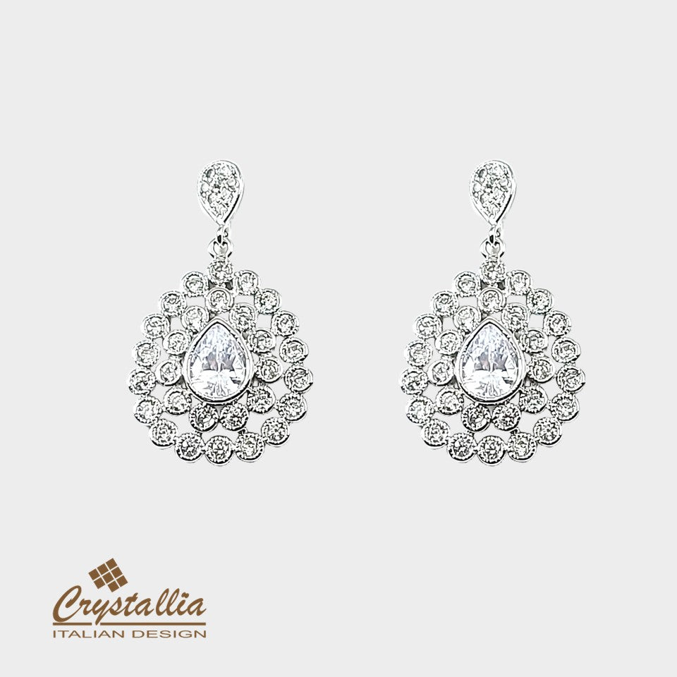 Pair of silver earrings with clear gemstones on a light gray background, featuring the Crystallia brand.